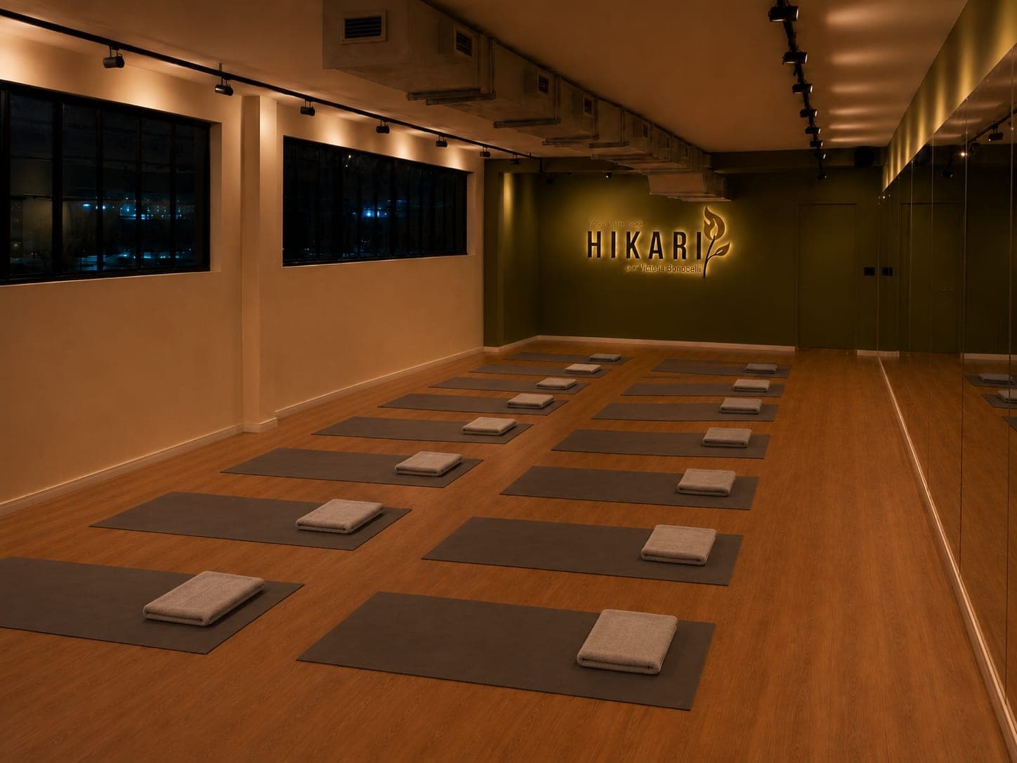 Sala de prática do Hikari com espelho, iluminação quente e tapetes prontos.